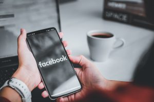 Hender som holder en mobil med facebook