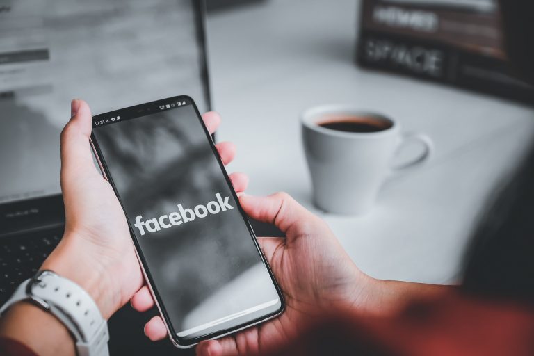 Hender som holder en mobil med facebook